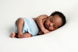 Sleeping newborn baby wearing light blue outfit lying on white background.