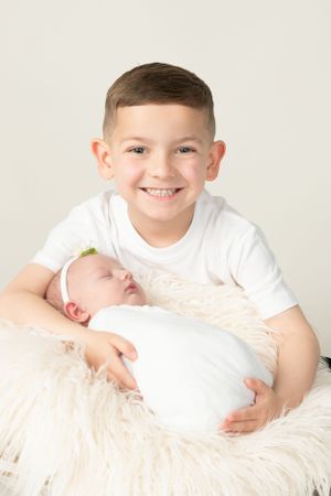 Two siblings posing together with baby on fluffy white blanket.
