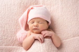 Sleeping baby wearing pink cap on soft pink blanket in newborn portrait.