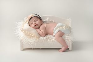 Peaceful newborn baby sleeping on miniature white wooden bed with soft textured bedding.