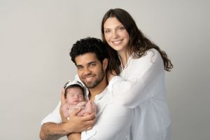 Studio portrait of family with newborn wearing white against grey background.