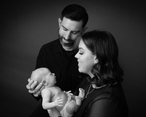 Intimate black and white portrait of new parents cradling their sleeping newborn.