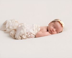 Sleeping newborn baby wrapped in cream lace swaddle with floral headband on white background.