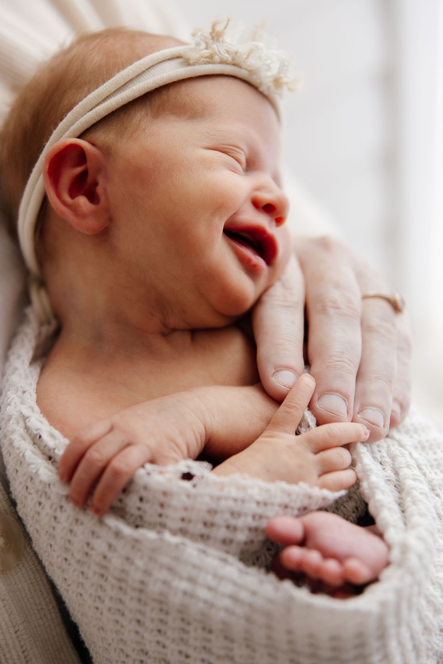 Newborn baby wearing delicate headband captured in soft natural light.