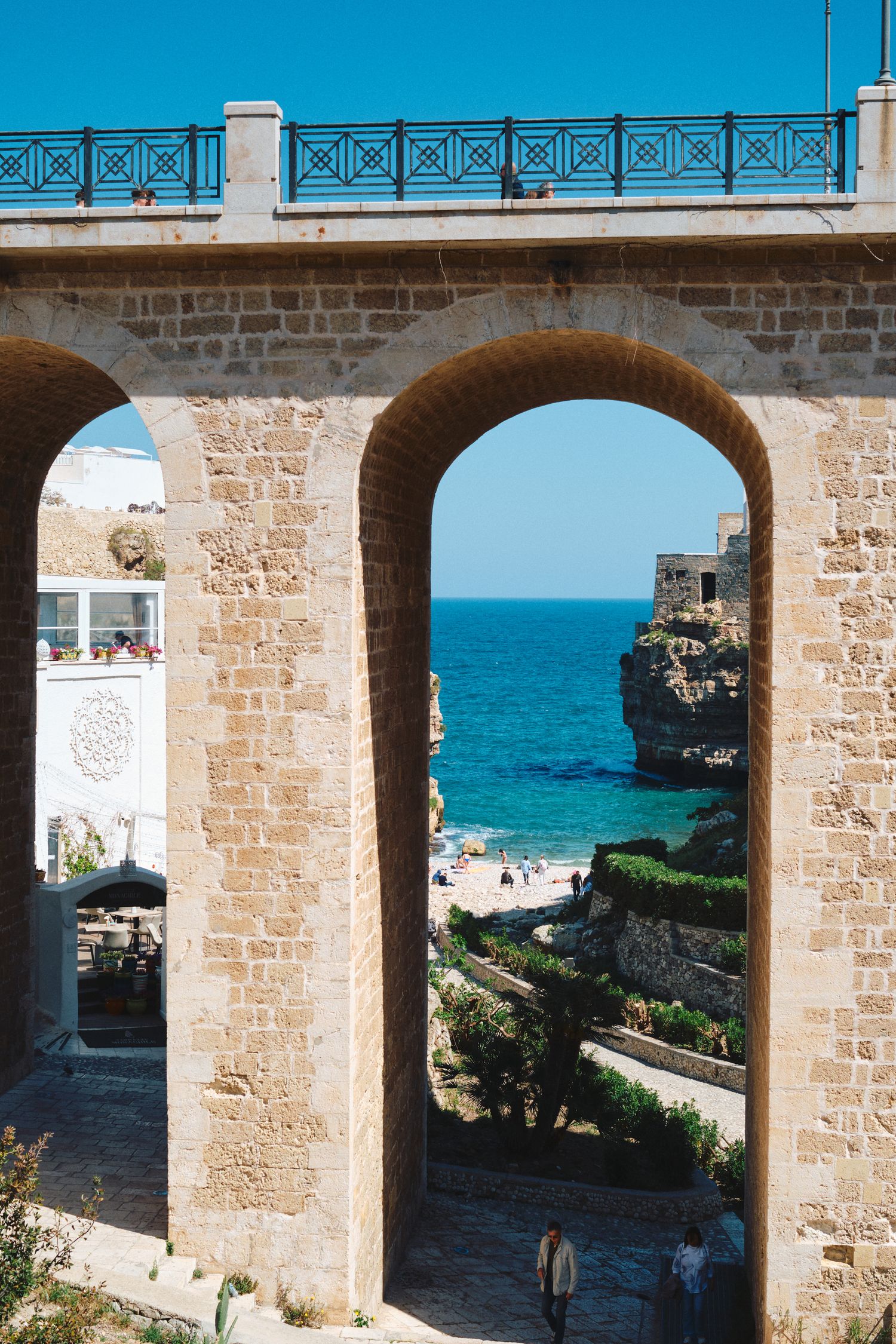 Stone archway bridge framing a scenic coastal beach view with blue Mediterranean waters.