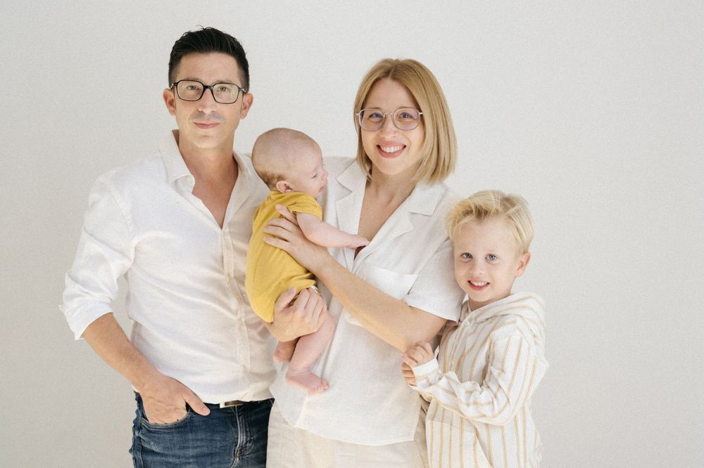 Retrato familiar moderno con padres e hijos con trajes blancos coordinados sobre un fondo claro.