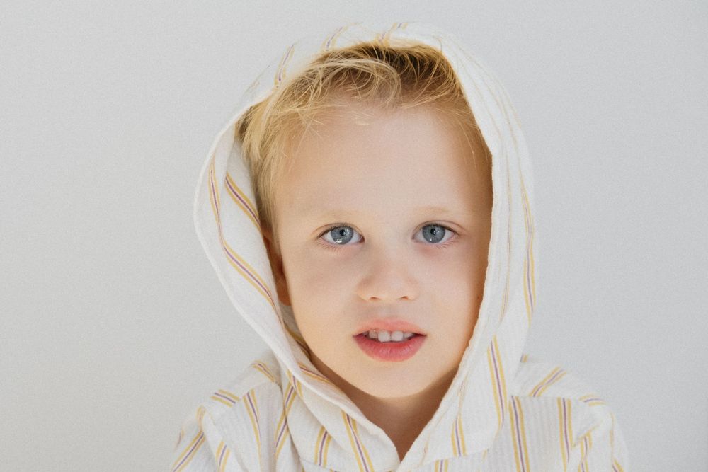 Primer plano de un niño con una sudadera con capucha blanca que mira directamente a la cámara con brillantes ojos azules.