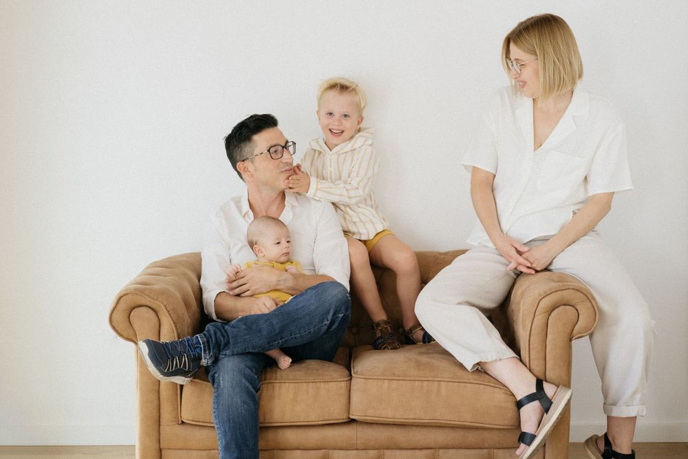 Familia sentada junta en un sofá marrón compartiendo un momento alegre.