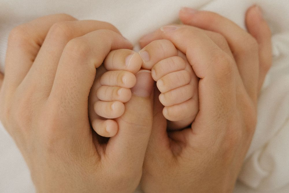Primer plano de pequeños pies de bebé sostenidos suavemente en manos de un adulto sobre un fondo blanco.