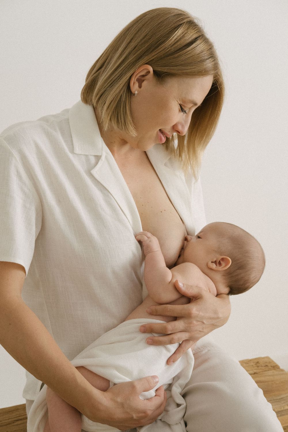 Momento íntimo de lactancia entre madre e hijo vestidos de blanco.