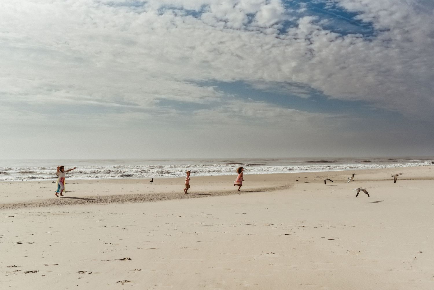 People enjoy a sunny day on a wide, pristine beach with scattered clouds overhead.