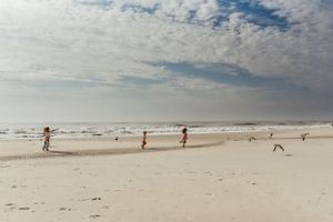 People enjoy a sunny day on a wide, pristine beach with scattered clouds overhead.