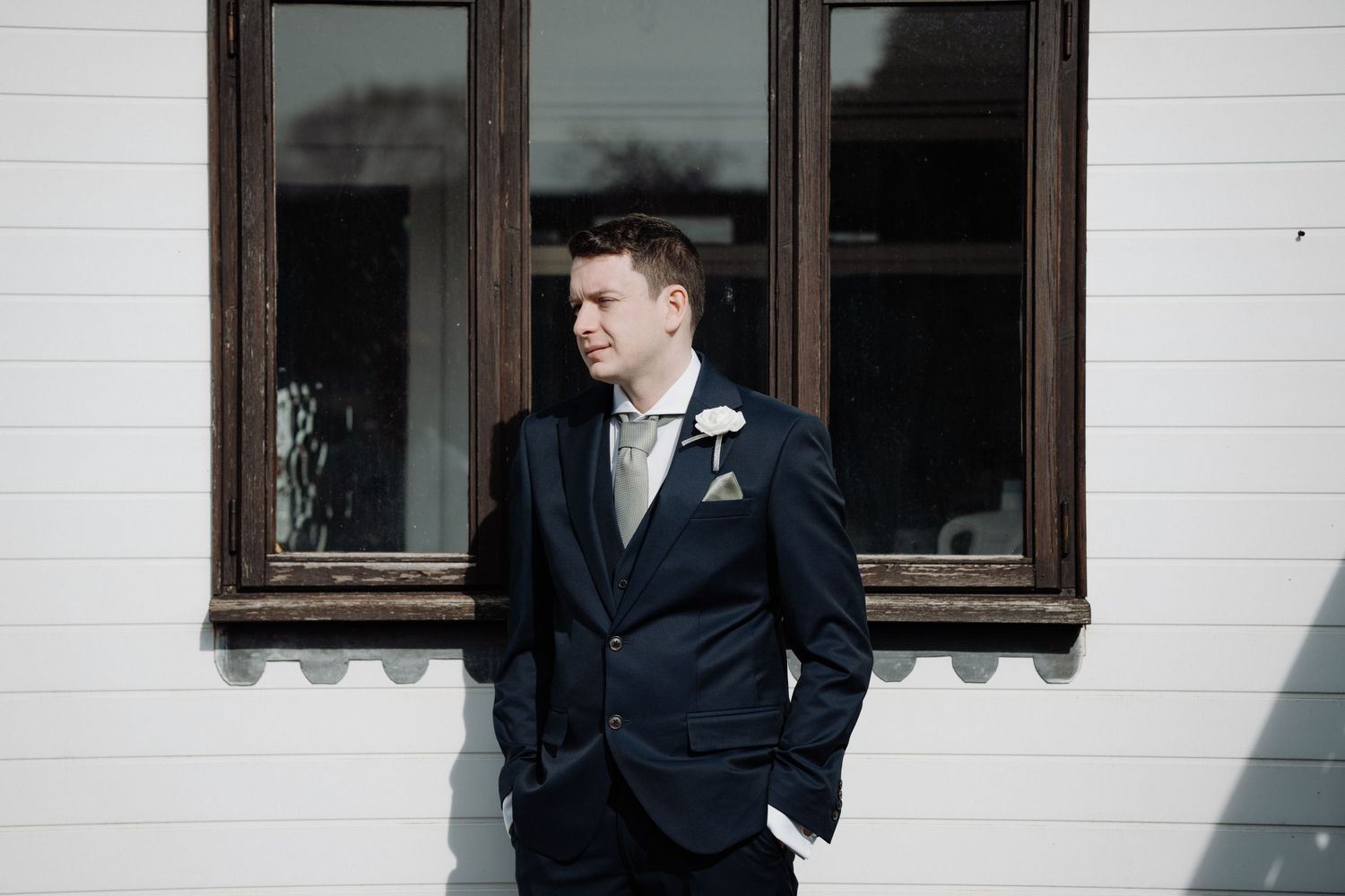 Formal groom portrait against white building exterior.