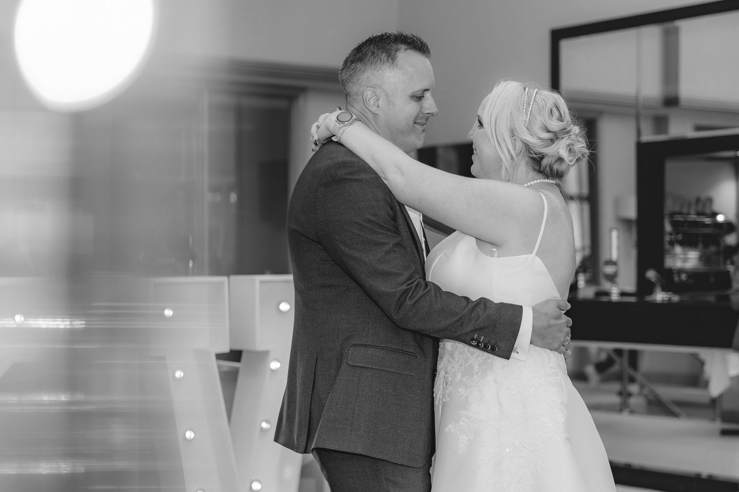 A black and white wedding photo captures a couple dancing in an indoor venue.