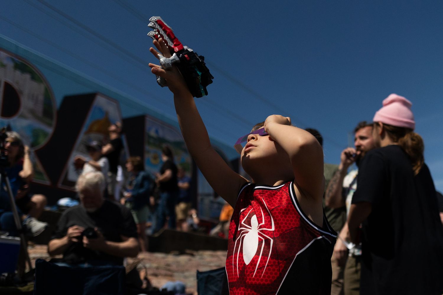 A person in a red Spider-Man shirt reaches joyfully toward the sky on a sunny day.
