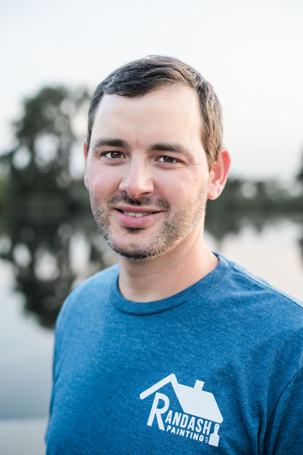 Outdoor portrait of person in blue company shirt by waterfront.