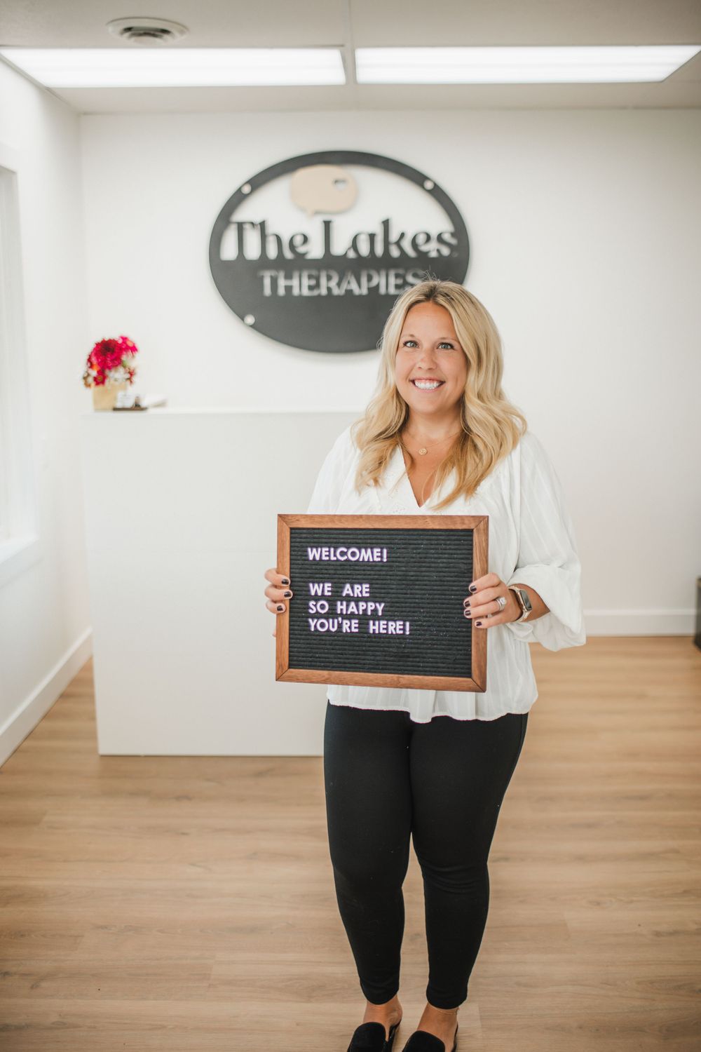 Therapist holds welcome sign board at The Lakes Therapies clinic entrance.
