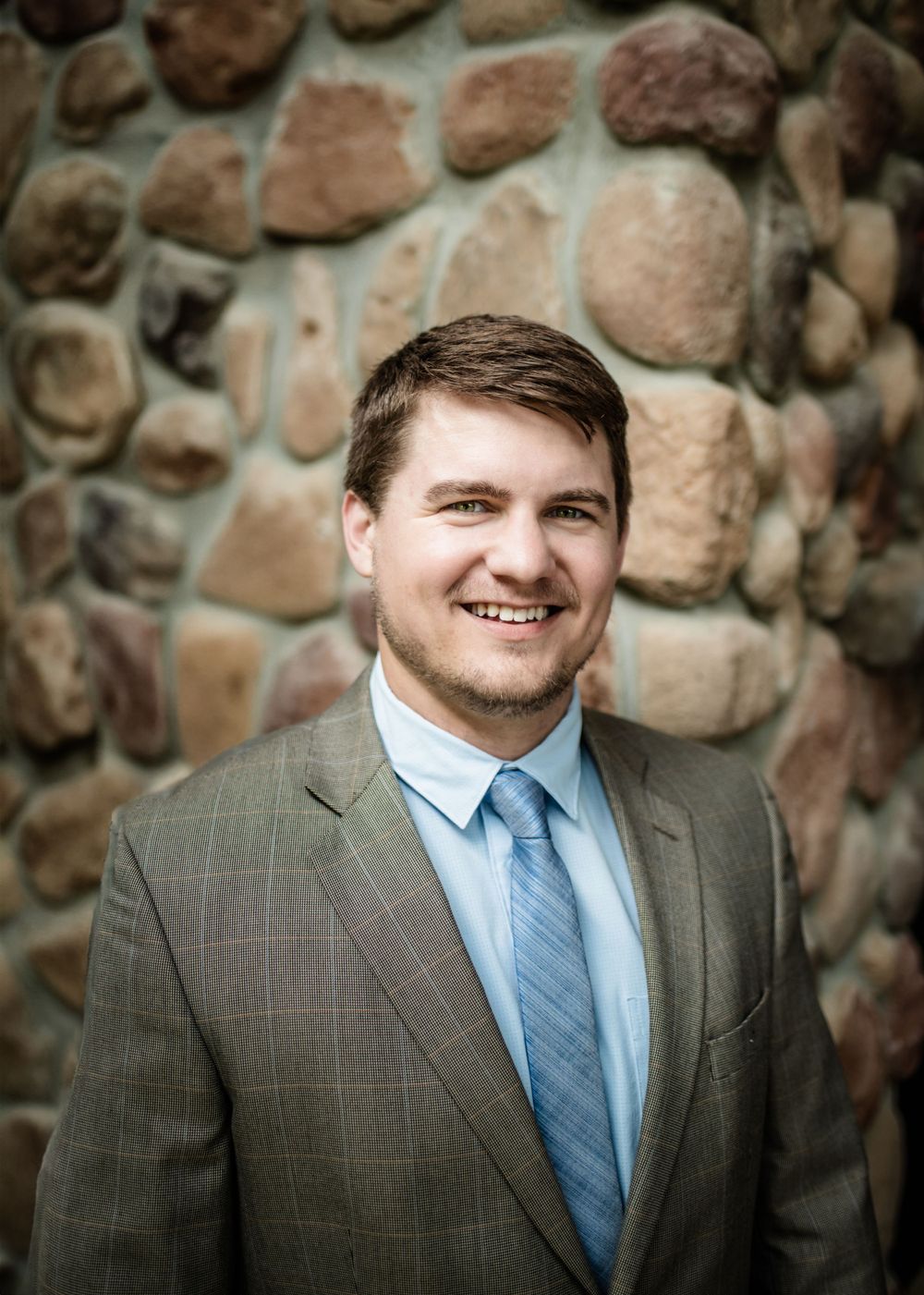 Business portrait of person in gray suit against stone wall background.