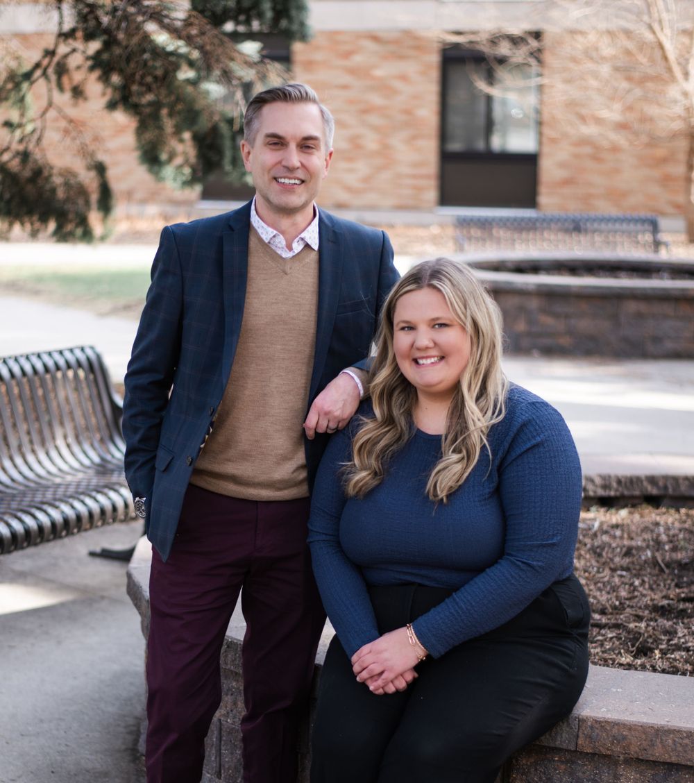 Two people sitting together on a bench in professional attire outside a brick building.