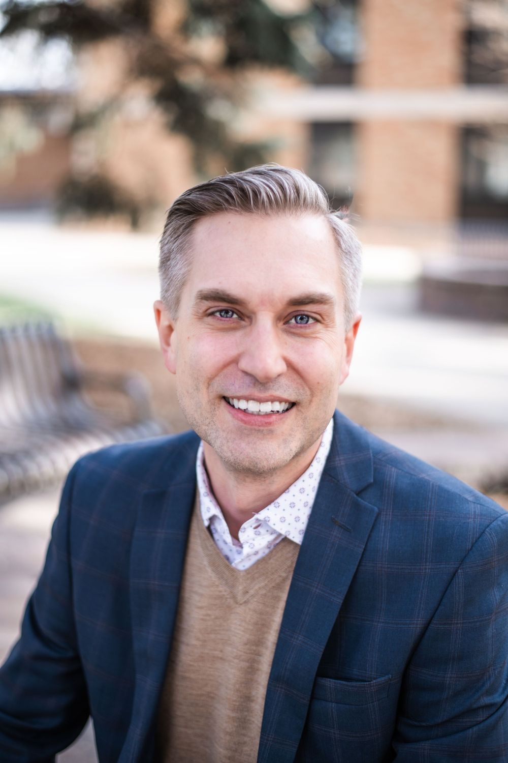 Professional headshot series of a person in a navy blazer and tan sweater outdoors.