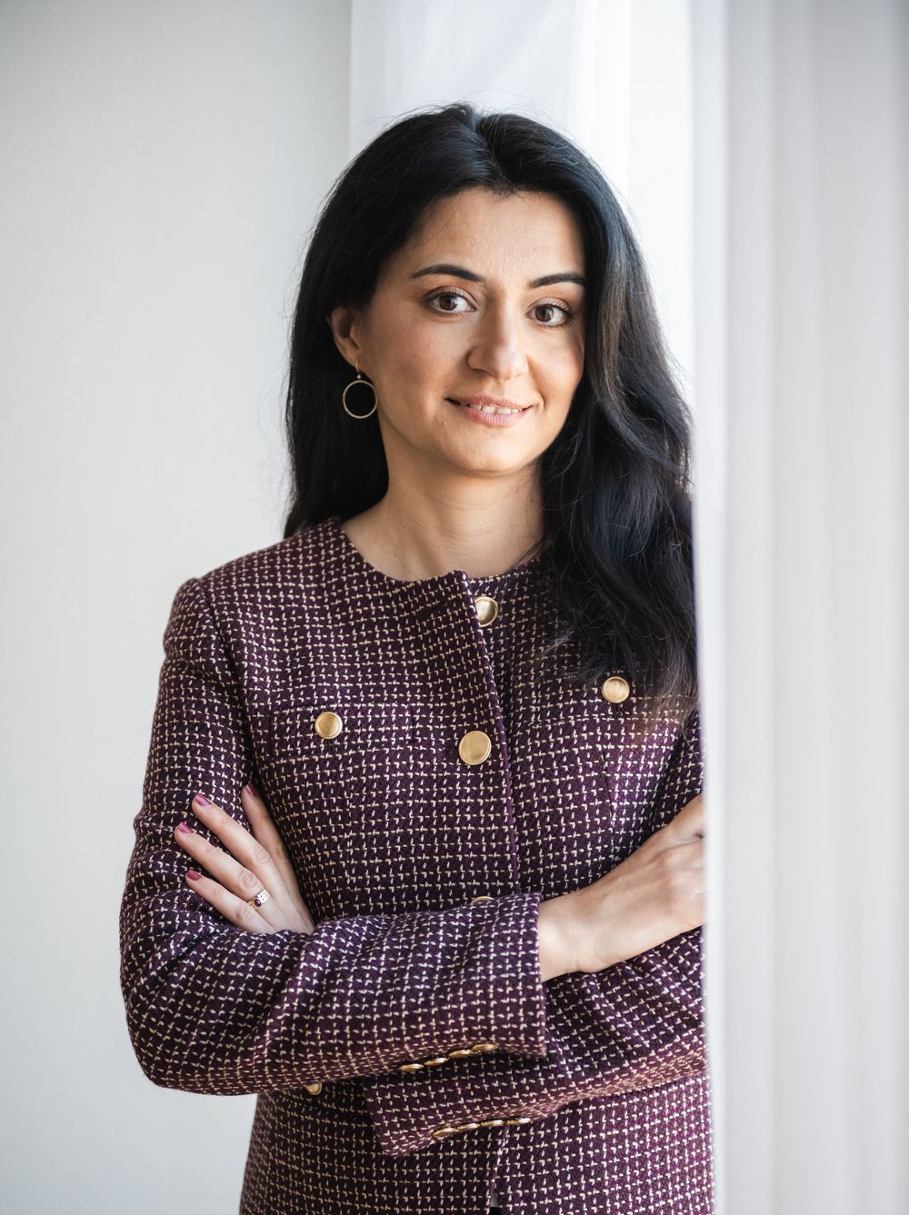 Woman in burgundy tweed jacket with gold buttons poses against white wall in four different casual poses.