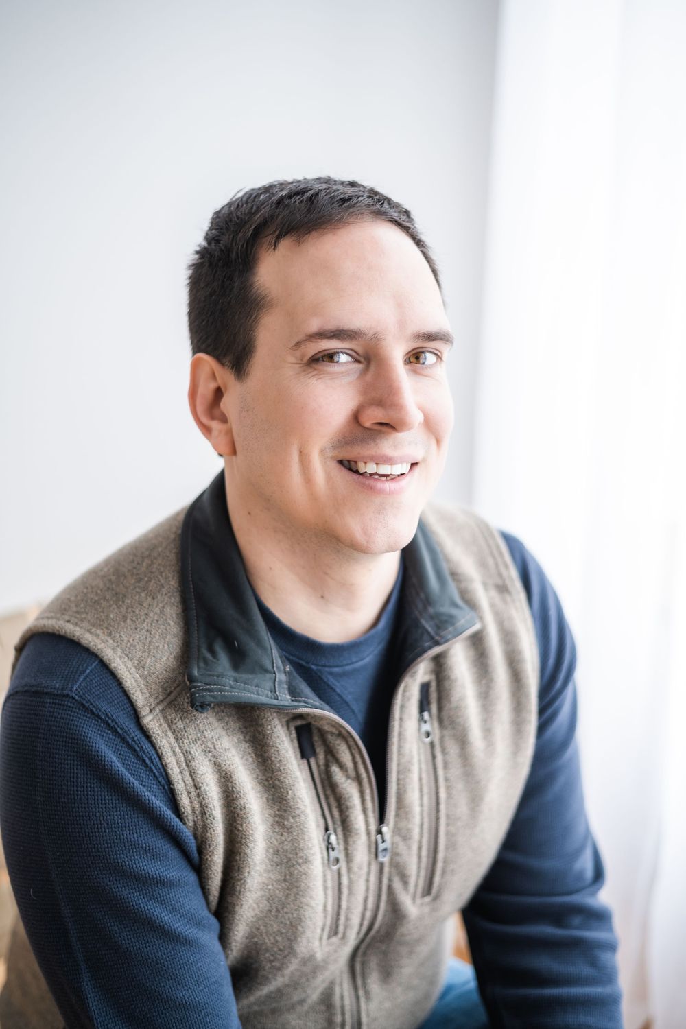 Professional headshot of person in fleece vest and navy sweater against white background.