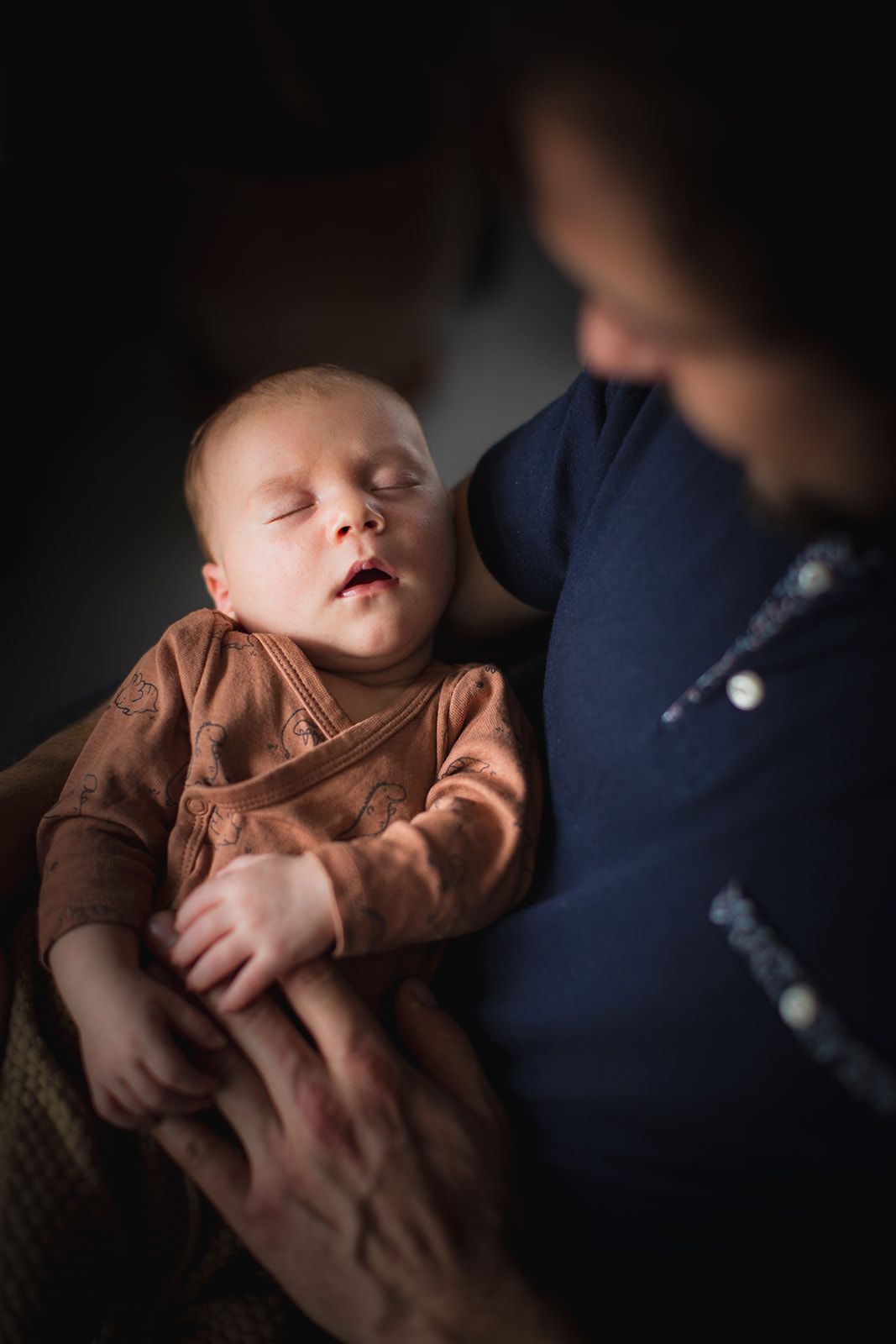 Bébé qui dort dans les bras de son père pendant une séance photo naissance à Sarlat