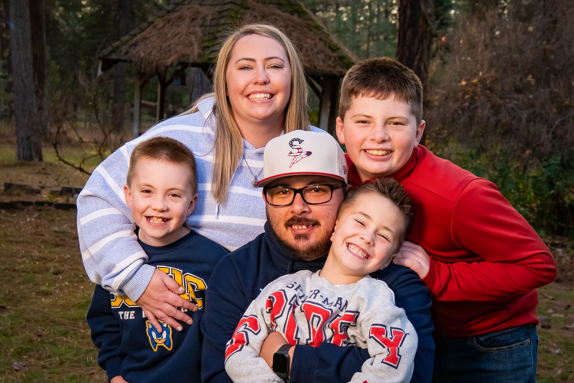 A family poses together outdoors in casual clothing against a wooded backdrop.