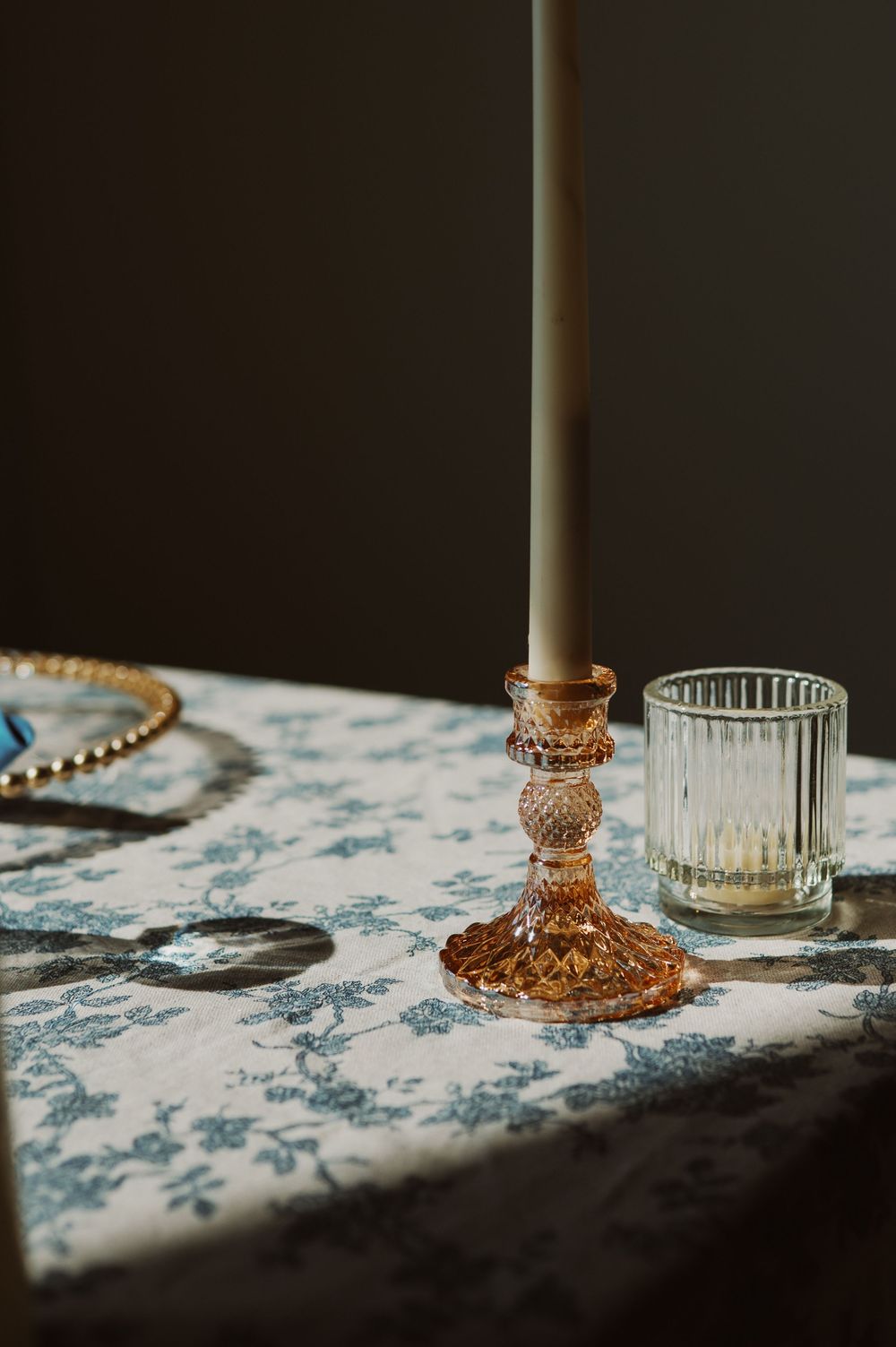 Vintage pink glass candlesticks and decorative holders arranged on a delicate floral tablecloth in soft lighting.