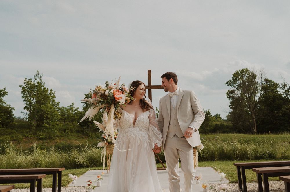 Romantic outdoor wedding ceremony setup with wooden benches and natural prairie landscape in the background.