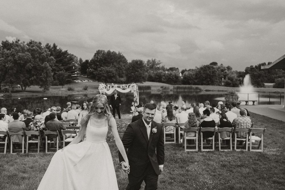 A panoramic black and white view of an outdoor wedding ceremony setup with white chairs arranged in rows on a grassy field.
