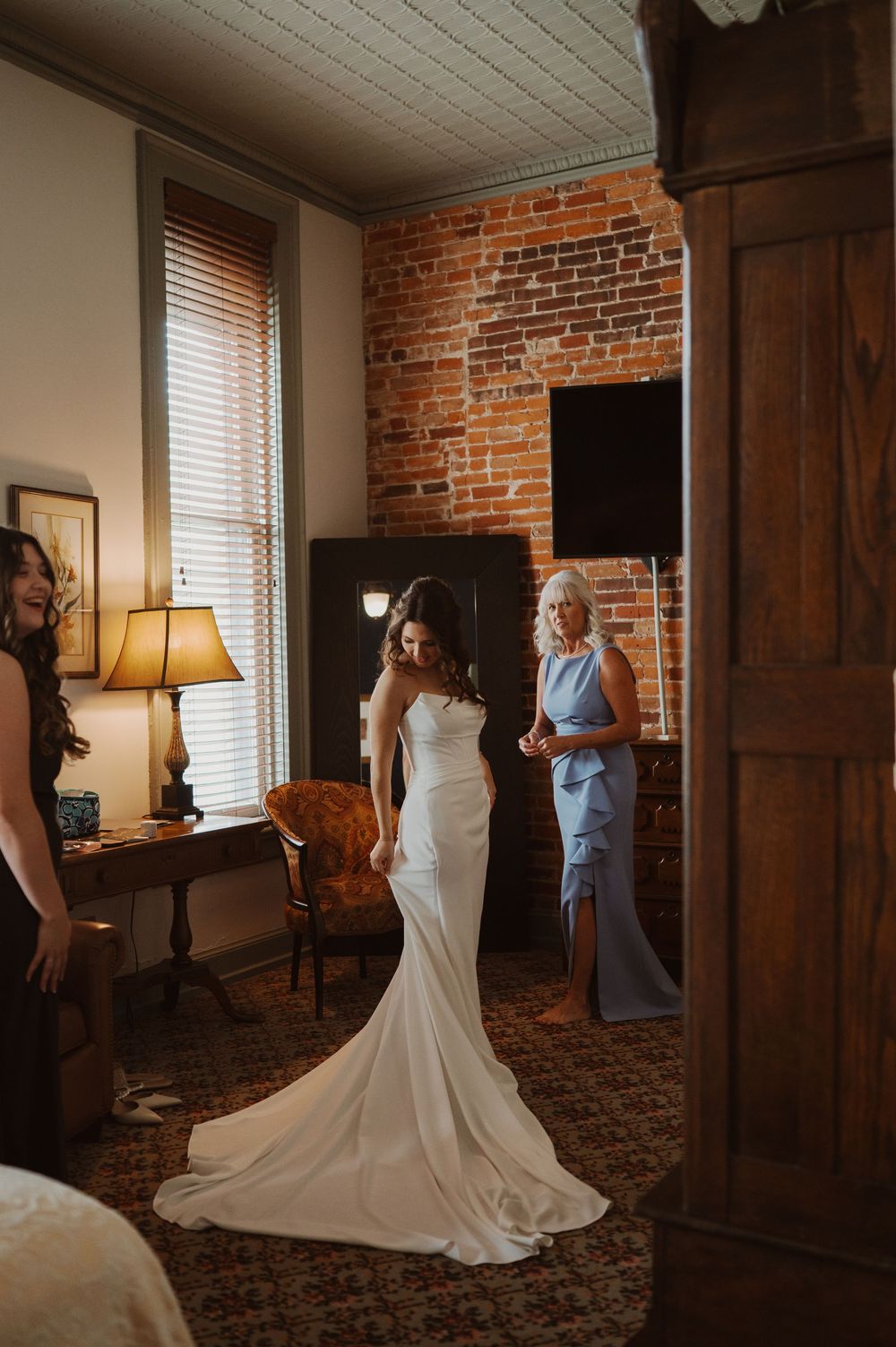 A series of wedding dress photos showing the back details and train of an elegant white gown in a rustic brick room.