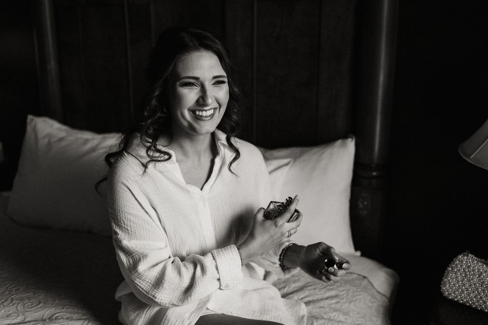 Black and white photo of someone relaxing on a bed in a white sweater while holding a phone and smiling.