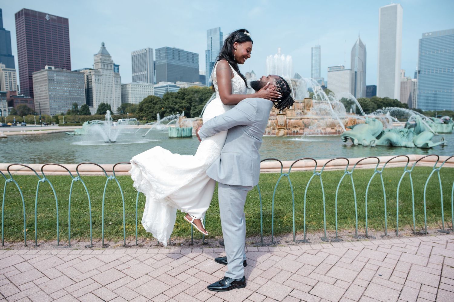 A couple in wedding attire embraces near Buckingham Fountain with Chicago's iconic skyline visible behind them.