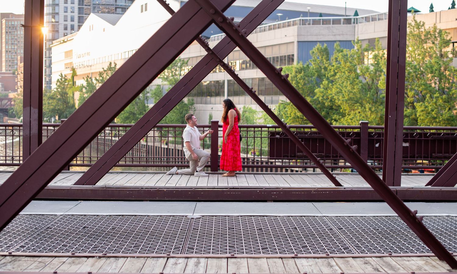 A wooden deck walkway with metal railings extends over an urban area during sunset, creating a scenic overlook.