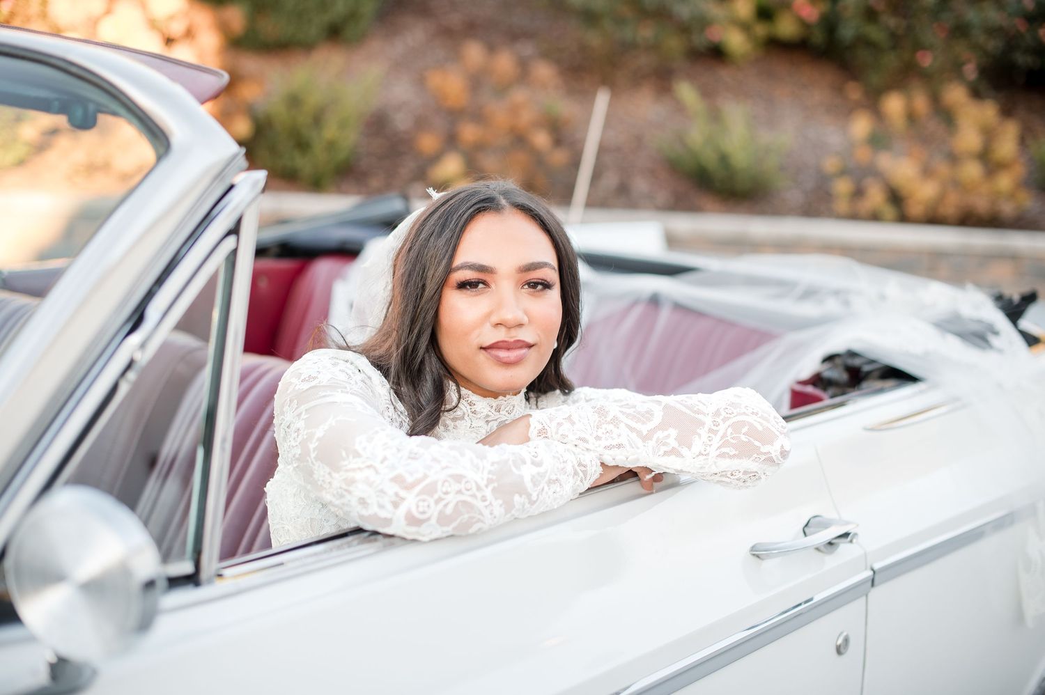 Someone in a white lace dress poses in a classic convertible car during an autumn photo session.