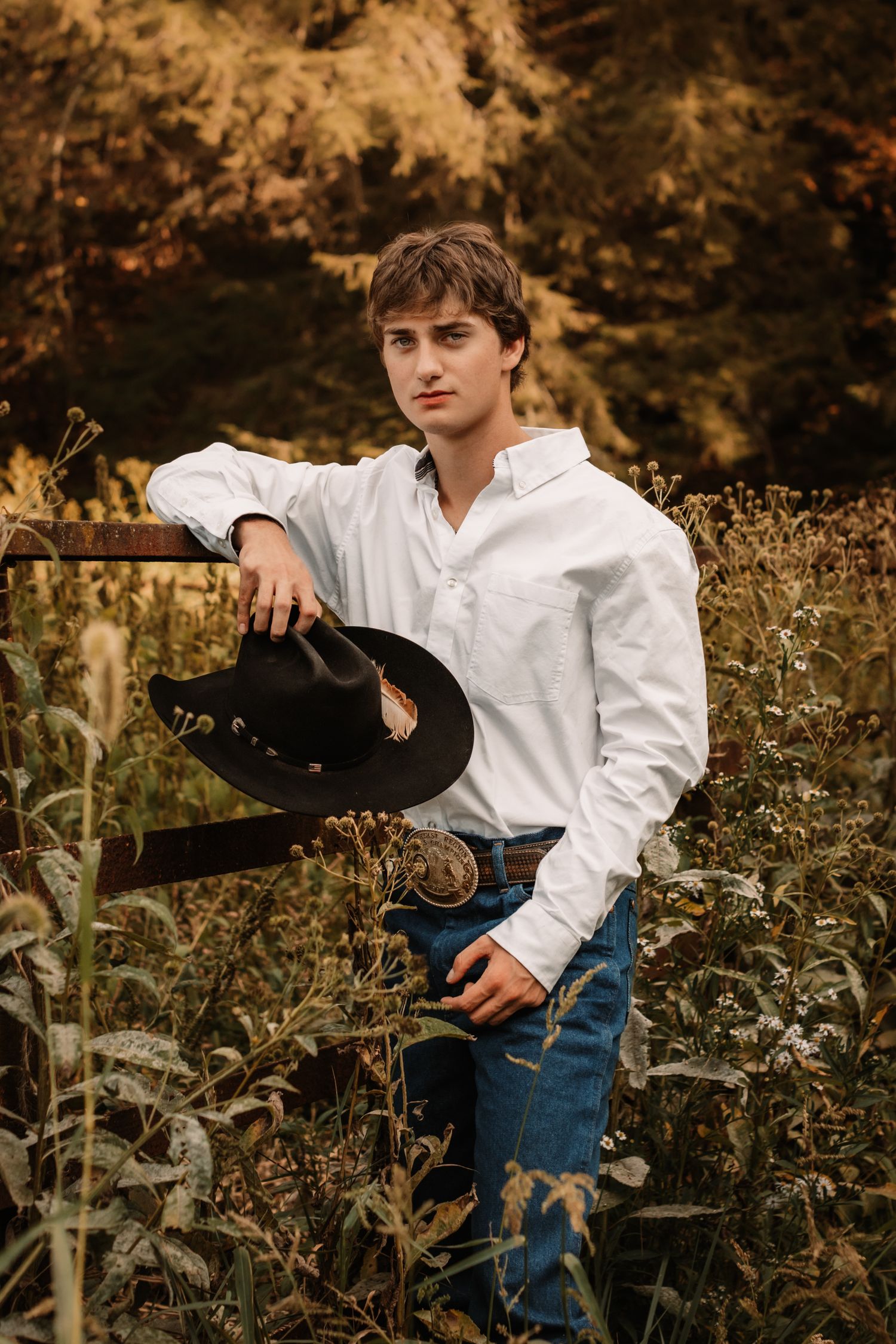 Person in white shirt and jeans poses casually among autumn wildflowers in outdoor photoshoot.