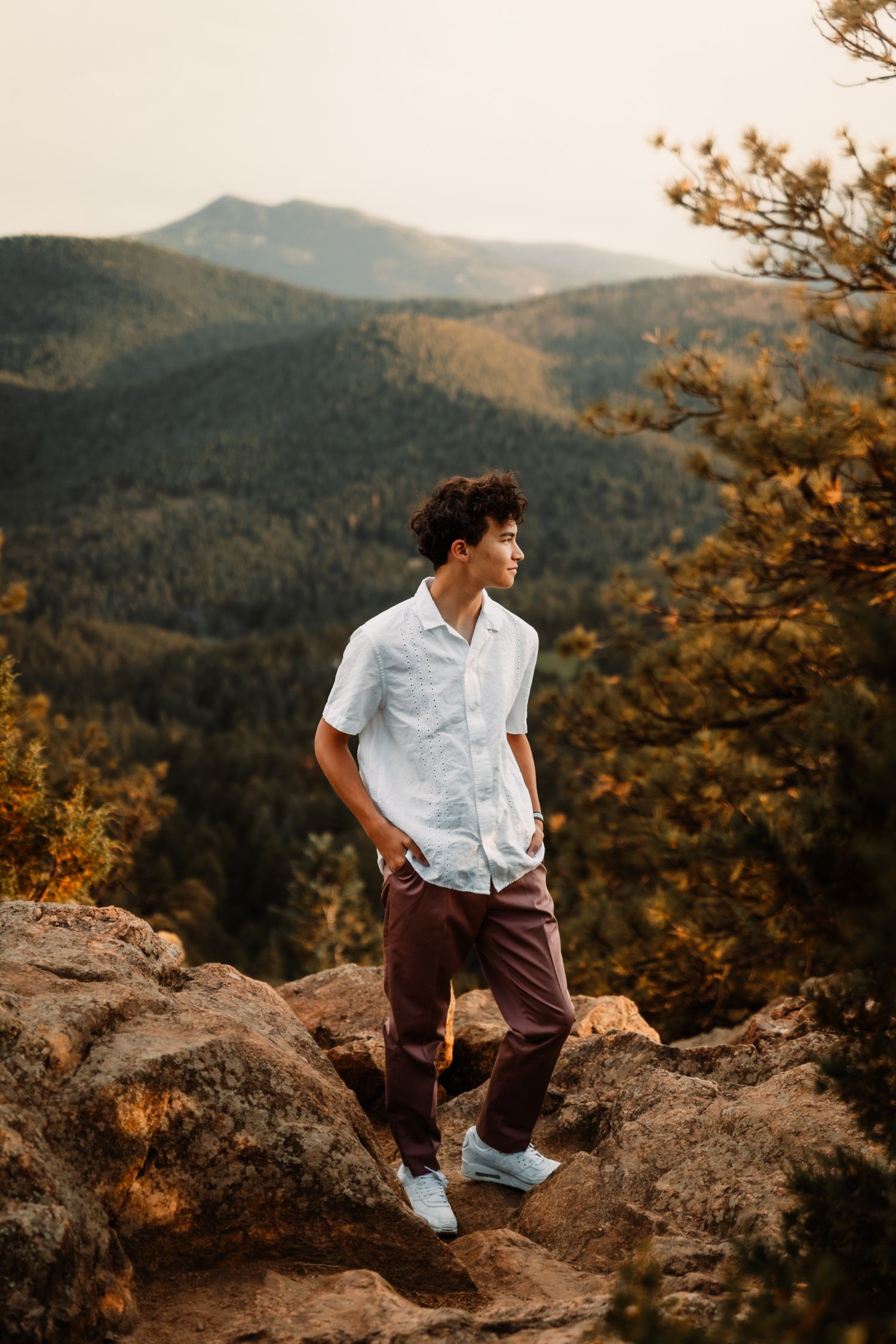 Young person stands on rocky overlook with scenic mountain vista in background.