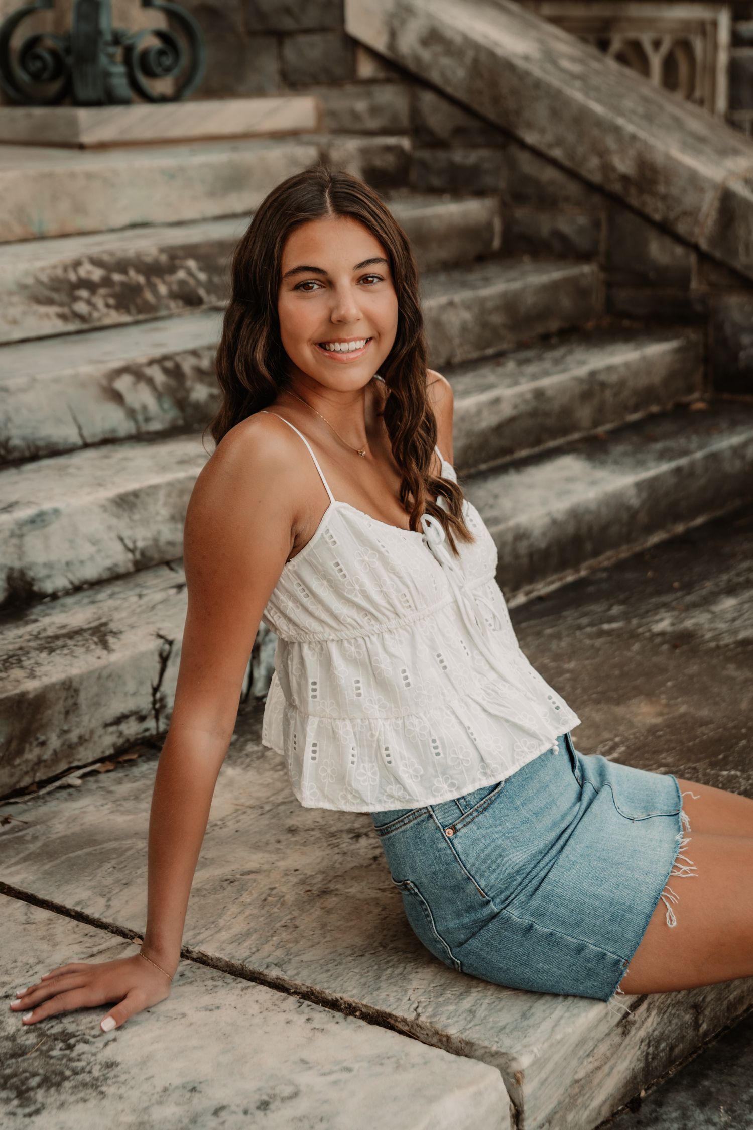 A woman in summer attire sits on stone steps during an outdoor portrait session.