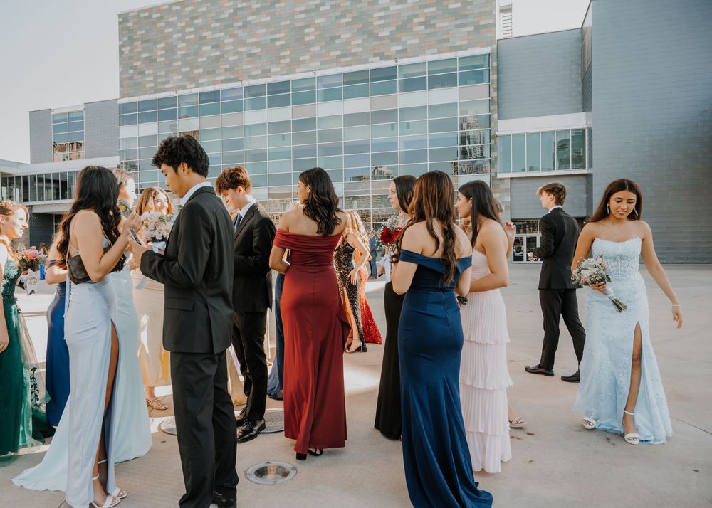 Elegantly dressed teens in formal gowns and suits gather outdoors before a prom event.