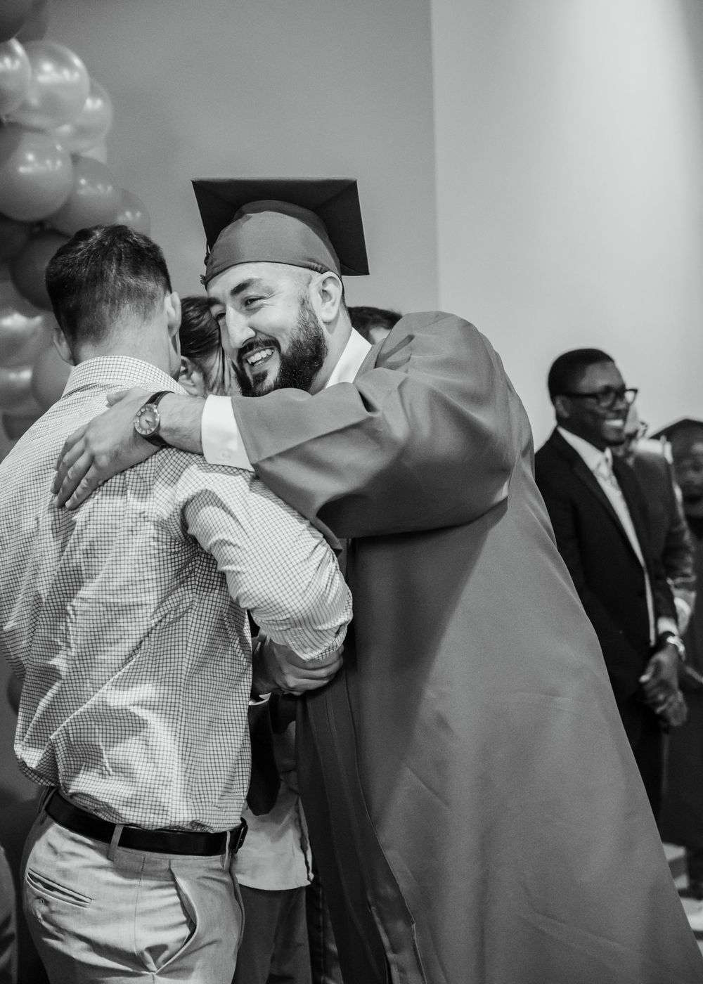 Graduate in cap and gown sharing a joyful hug with a guest at a graduation celebration.