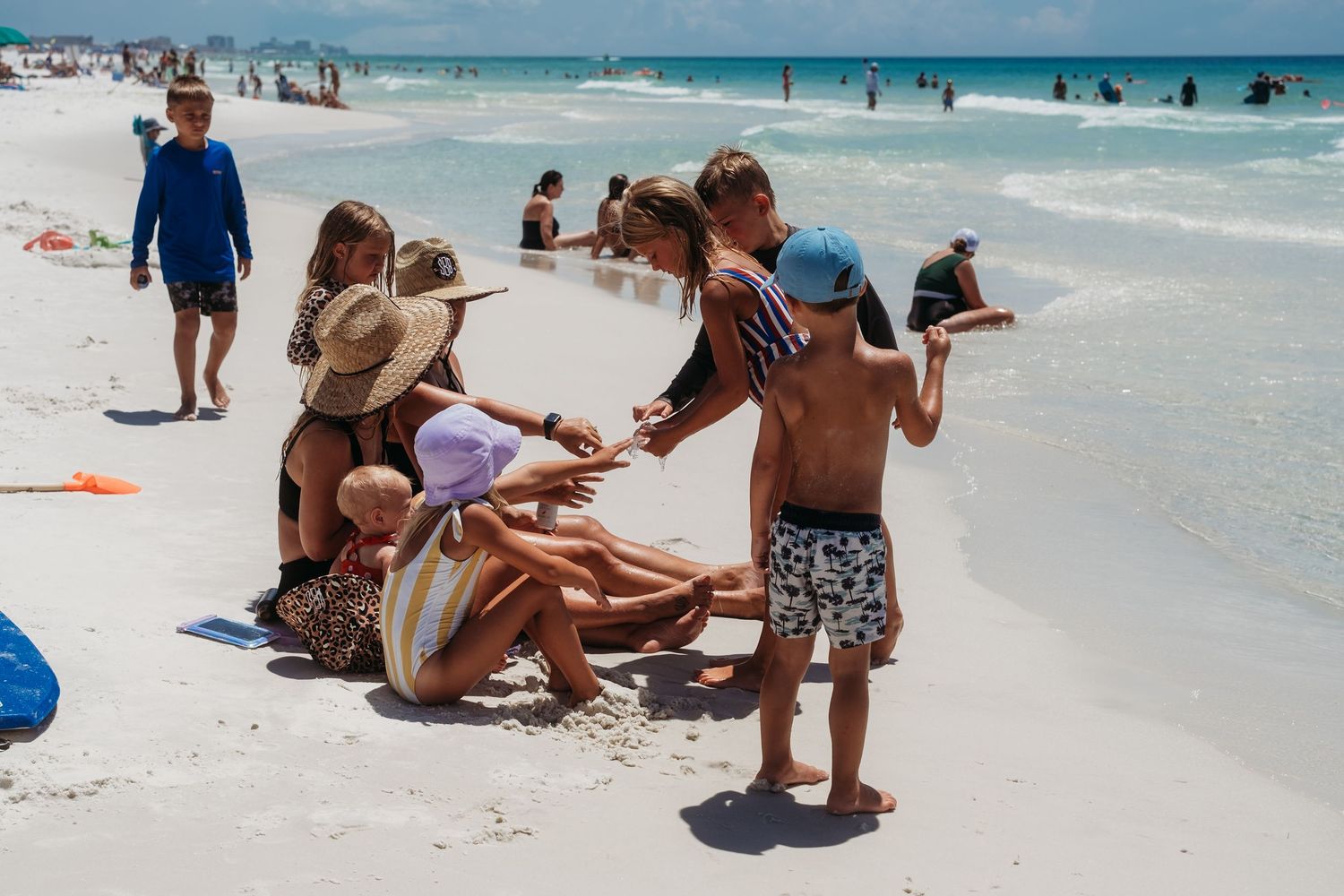 Beachgoers relax and play in the white sand as turquoise waves crash along a tropical shoreline on a sunny day.