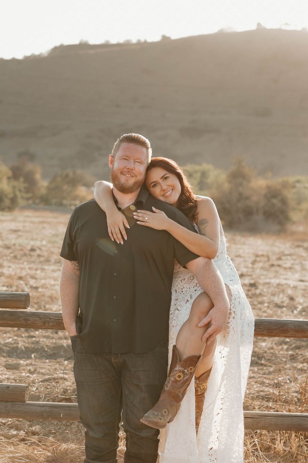A couple poses together in golden sunlight on a hillside during their romantic sunset engagement photo session.