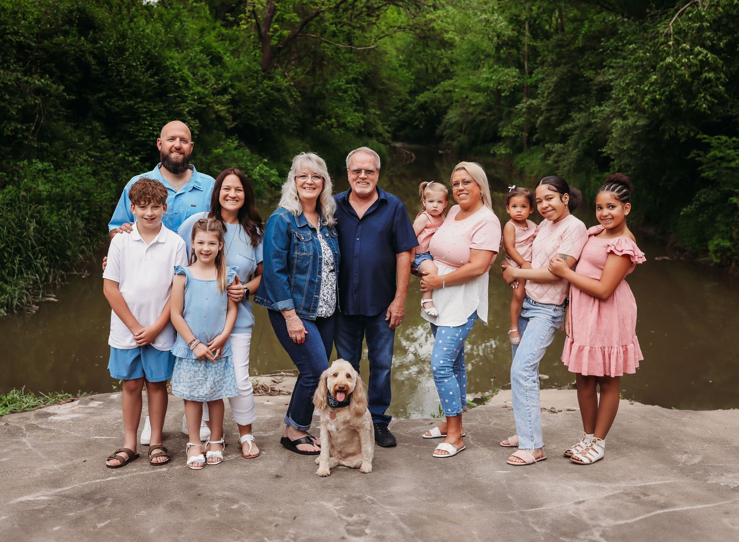Extended family group photo with a dog standing together on a path near water.
