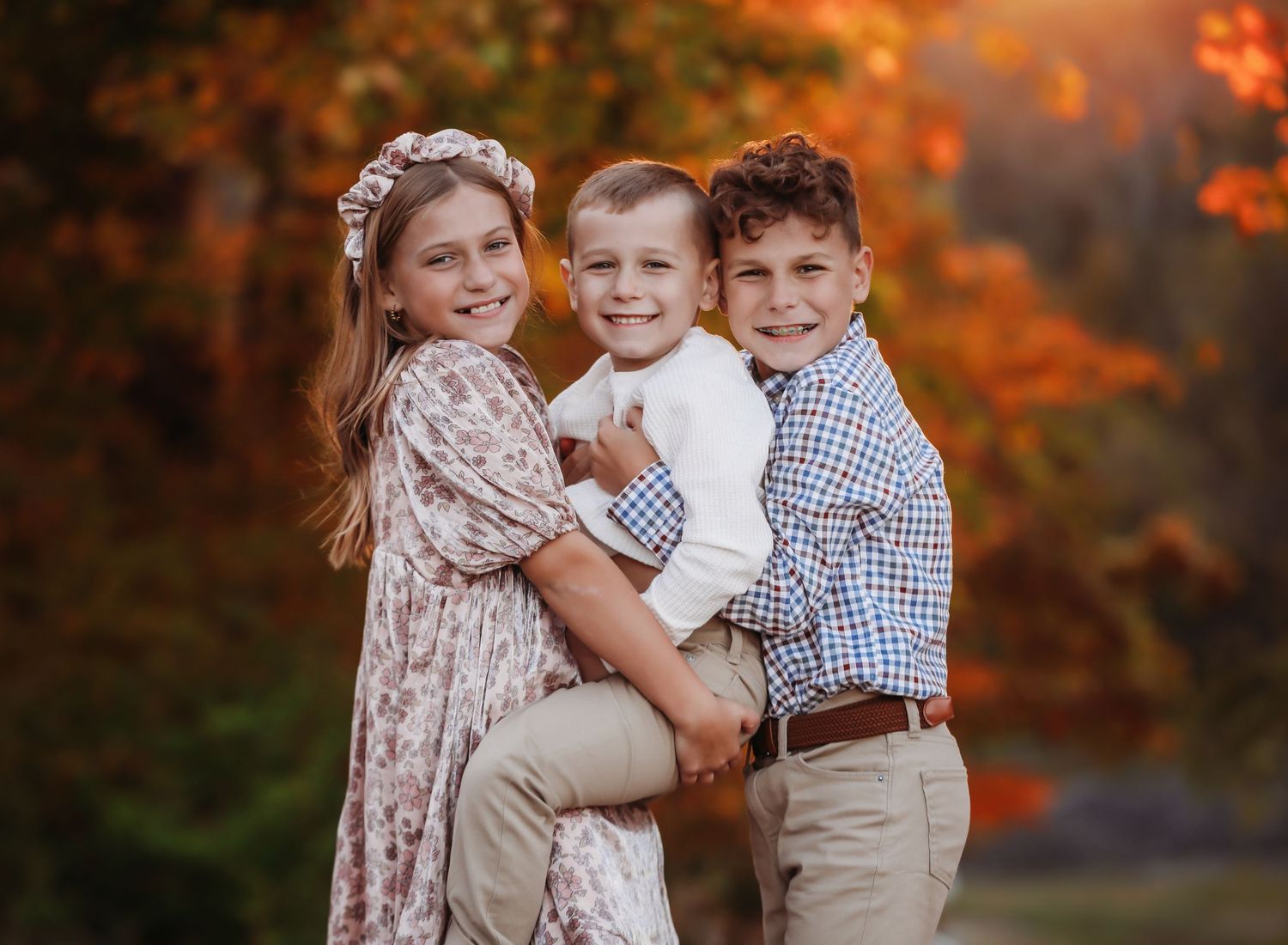 Three children with the smallest one being held in fall scenery.
Best child photographer, Peoria, IL.