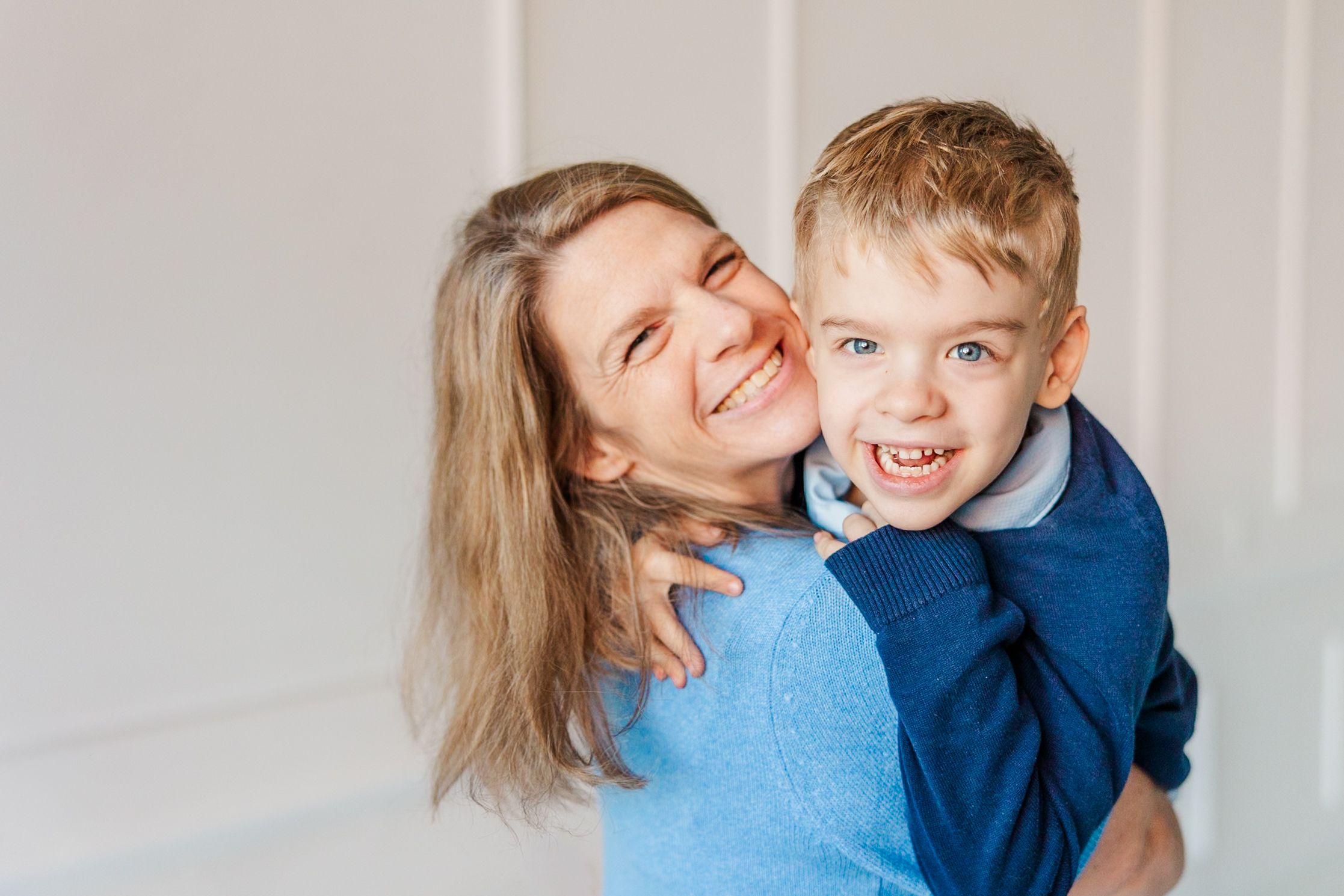 Playful family moment captured against white wall in casual clothing.