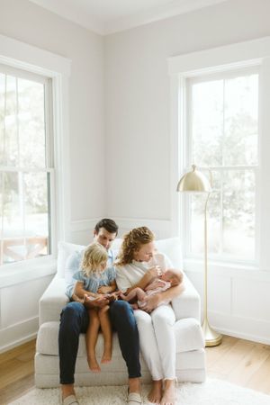Photo by B.Logsdon of a family sitting together on a white couch in a bright corner room with large windows in Savannah, Georgia.