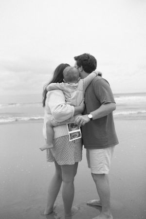 Photo by B.Logsdon of a family embracing on Hilton Head Island beach while holding an ultrasound photo in black and white.