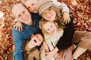Photo by B.Logsdon of a happy family huddling close together for a playful photo while lying in the autumn leaves.