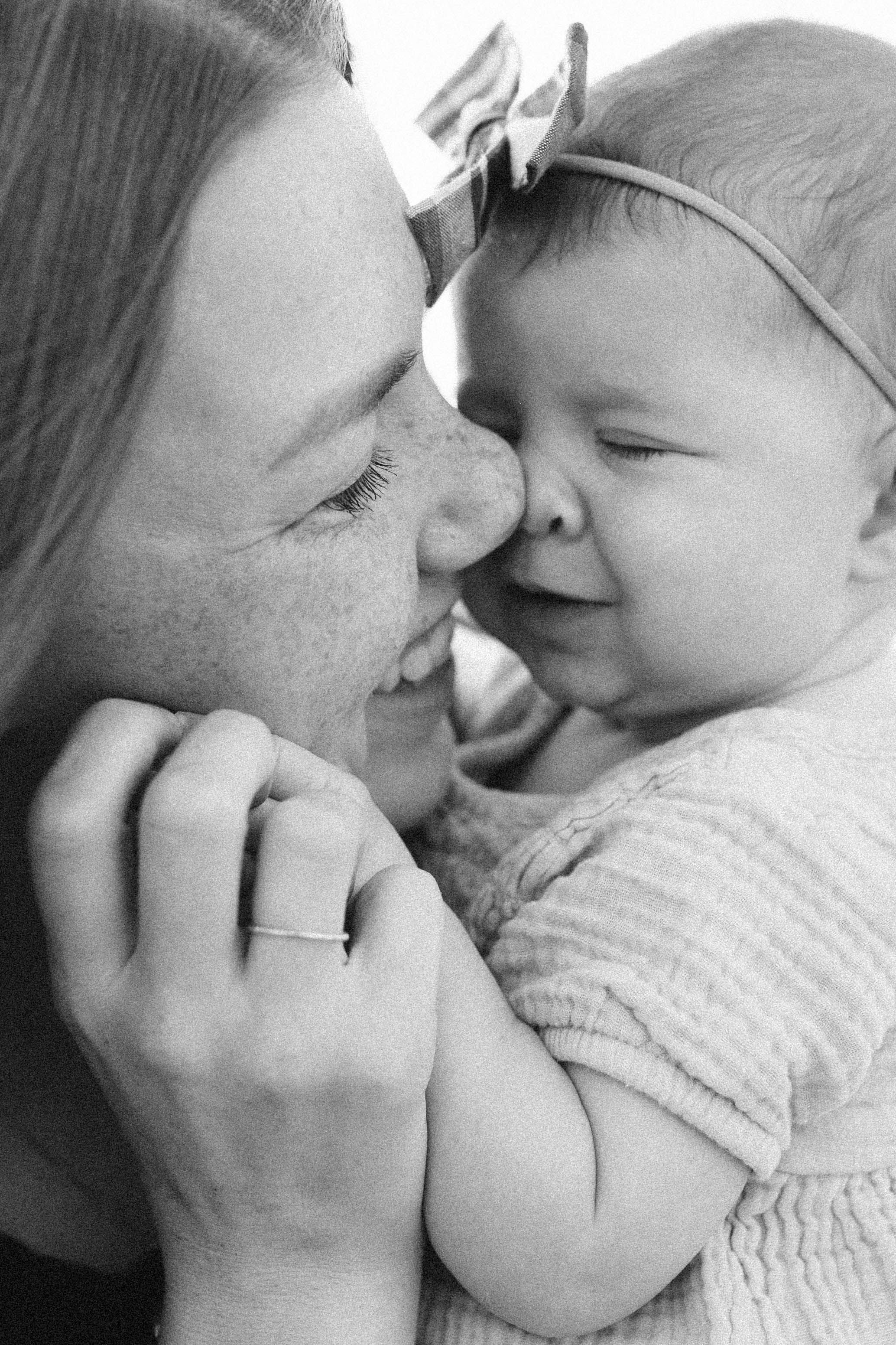 A tender black and white close-up photo by B. Logsdon Photography of a loving moment between a mother and baby smiling together.